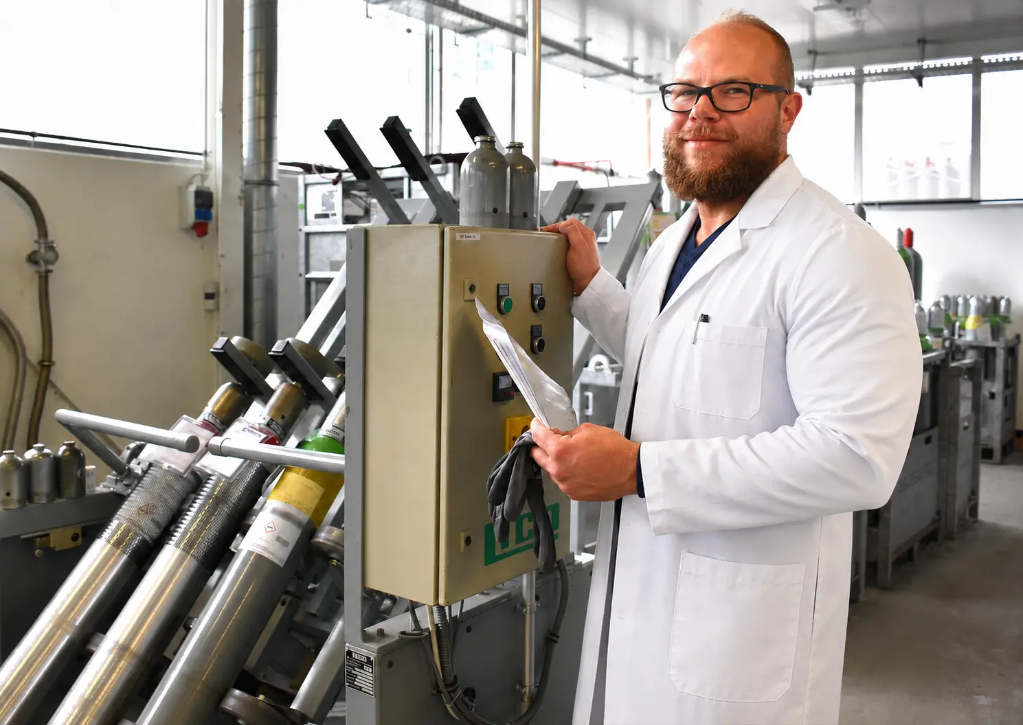 Der Laborleiter von Kraiss & Friz im Laborkittel am Abfüllstand für Prüf- und Laborgase, im Hintergrund Gasflaschen im Gestell